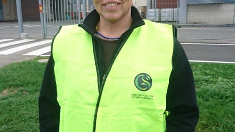 Bild på skyddsombudet Sanna Levinsson framför sin arbetsplats iförd varselväst.