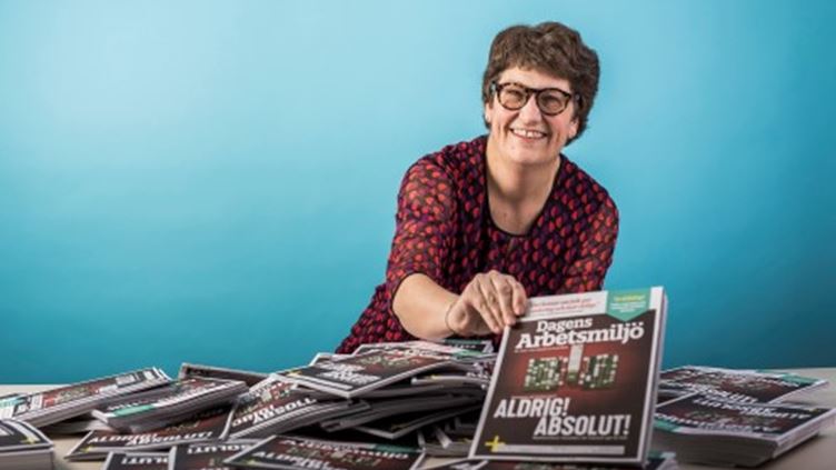Helle Klein sitter bakom ett bord som är fyllt med tidningsexemplar av tidningen Dagens Arbetsmiljö.
